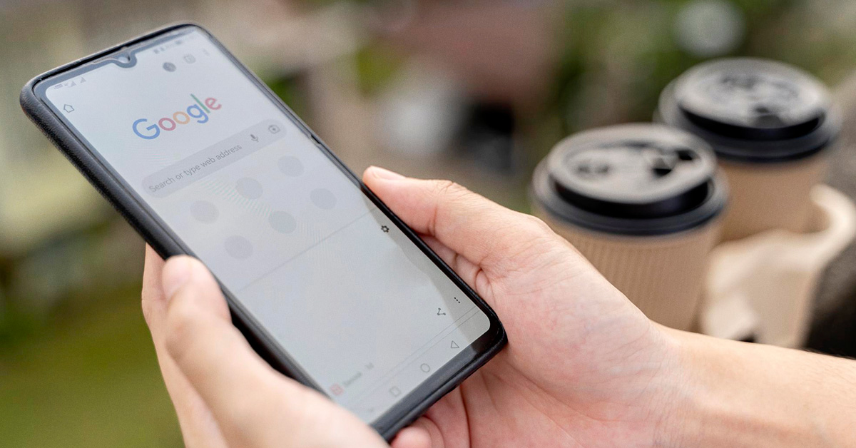 mãos segurando um smartphone com a tela de pesquisa do Google